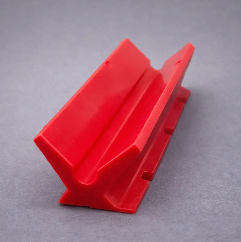Red polyurethane V-block wear pad and slide component on grey background.